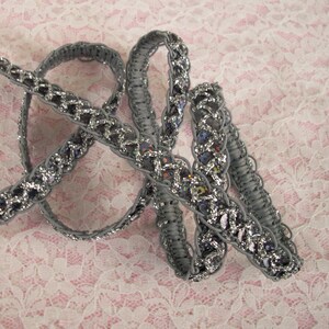 May include: Silver and gray braided trim with a sparkly finish. The trim is made of a woven fabric with a delicate pattern.