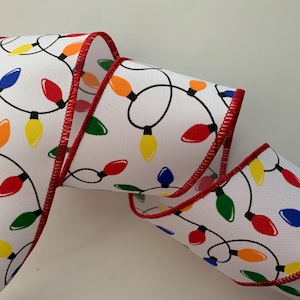 May include: White ribbon with a repeating pattern of colorful Christmas lights in red, yellow, green, blue, and orange. The ribbon has a red stitched edge and is ideal for holiday crafts and decorations.