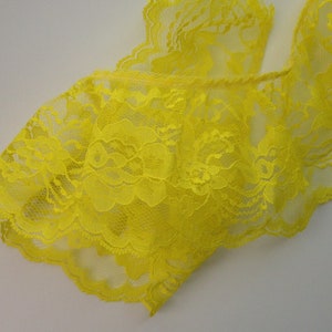 May include: Close-up of a bright yellow lace garment. The delicate fabric features intricate floral patterns and scalloped edges. The lace is a vibrant, sunny yellow color, and the garment appears to be lingerie or a similar delicate item.