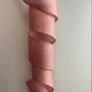 May include: A pink, glittery ribbon with a textured, woven design. The ribbon is curled into a spiral shape.