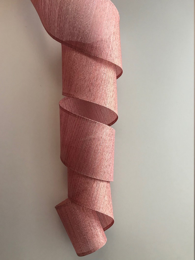 May include: A pink, glittery ribbon with a textured, woven design. The ribbon is curled into a spiral shape.