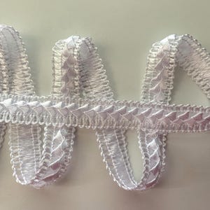 May include: White braided trim with a decorative pattern. The trim is made of a soft, silky material and has a delicate, intricate design.