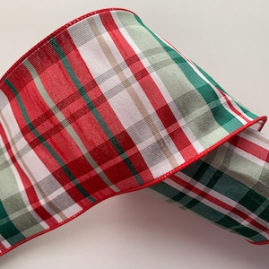 May include: A wide, decorative ribbon with a plaid pattern in red, green, white, and tan. The ribbon has a red stitched edge. This festive ribbon is suitable for holiday and craft projects.