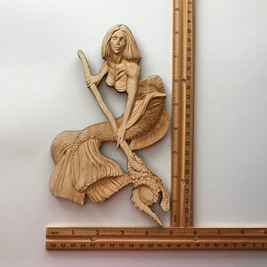 May include: A wooden carving of a mermaid holding a trident. The mermaid has long flowing hair and a detailed tail. The carving is approximately 17 inches tall.