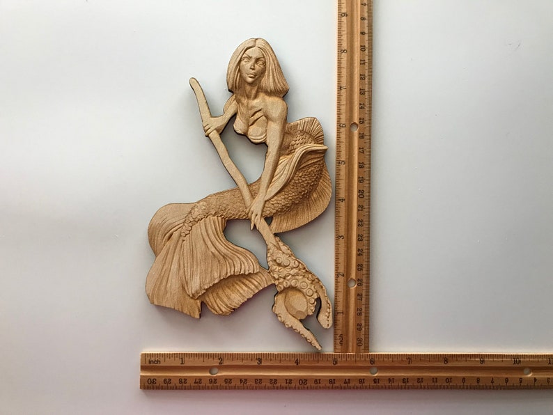 May include: A wooden carving of a mermaid holding a trident. The mermaid has long flowing hair and a detailed tail. The carving is approximately 17 inches tall.