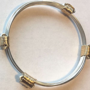 以下が含まれることがあります： 4つの金のアクセントが付いた銀のバングルブレスレット。ブレスレットは複数のワイヤーでできています。