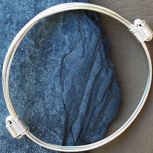 Puede incluir: Un brazalete de plata con un diseño de alambre trenzado en cada extremo.