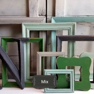 May include: A collection of various sized, distressed wooden picture frames in shades of green, gray, and brown. A large, dark gray letter "N" leans against the frames. A small sign with the word "Mix" is visible.