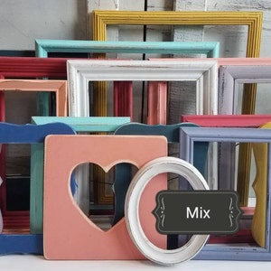 May include: A collection of colorful, empty picture frames in various shapes and sizes. The frames are painted in shades of blue, pink, yellow, green, and white. Some frames have heart-shaped cutouts, while others are oval or rectangular.