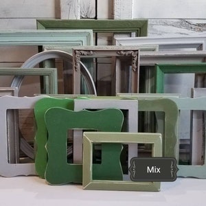 May include: A collection of various picture frames in shades of green and white. The frames are in different shapes and sizes, some with ornate details. The word "Mix" is on a small label. The frames are arranged against a white wooden background.