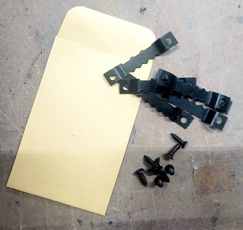May include: A collection of black sawtooth picture hangers, screws, and a tan envelope. The hangers have a zigzag edge and a hole for mounting. The screws are small and black. The envelope is rectangular.