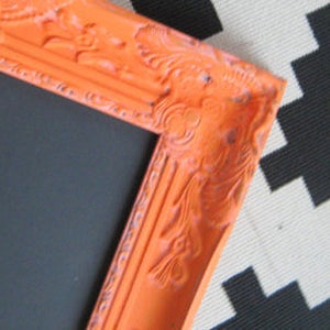 Peut inclure: Gros plan sur un coin d'un cadre photo orange avec des d&eacute;tails orn&eacute;s. Le cadre a une finition vieillie et un int&eacute;rieur noir. Le cadre est pos&eacute; sur un fond &agrave; motifs noir et blanc.