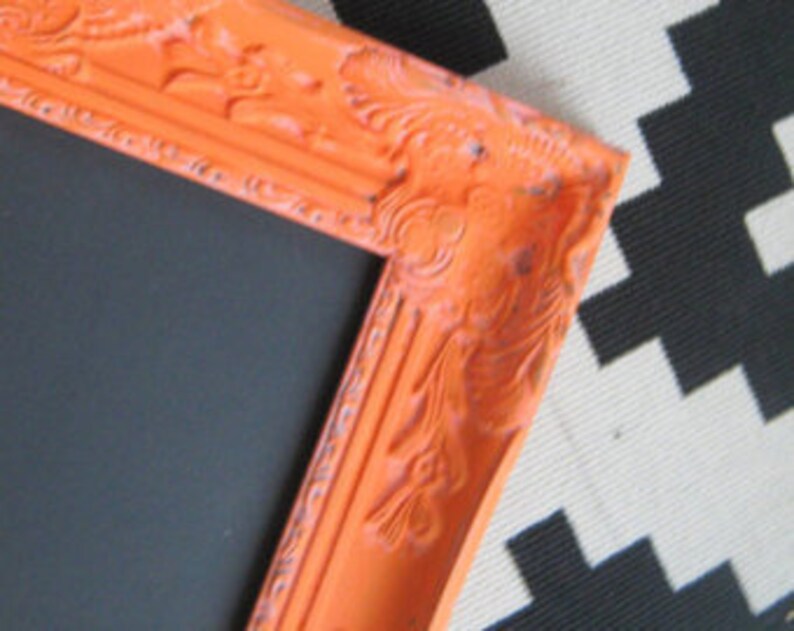 Peut inclure: Gros plan sur un coin d'un cadre photo orange avec des d&eacute;tails orn&eacute;s. Le cadre a une finition vieillie et un int&eacute;rieur noir. Le cadre est pos&eacute; sur un fond &agrave; motifs noir et blanc.
