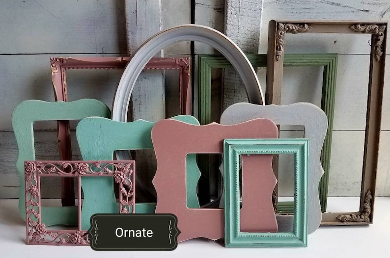 May include: A collection of colorful, empty picture frames in various shapes and sizes. The frames are painted in shades of pink, green, and white. One frame has the word "Ornate" on it. The frames are arranged in front of a light blue background.