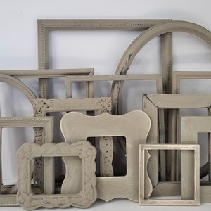 May include: A collection of various gray picture frames in different shapes and sizes. The frames include square, rectangular, and circular designs, some with ornate detailing. The frames are arranged in a layered composition, creating a vintage aesthetic.