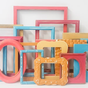 May include: A collection of assorted picture frames in various shapes and sizes, featuring a palette of pink, blue, yellow, and tan colors. The frames include rectangular, oval, and heart-shaped designs with smooth, textured, and ornate finishes.