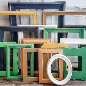 May include: A collection of various wooden picture frames in different shapes and sizes. The frames are painted in a variety of colors, including green, yellow, black, and white. Some frames are rectangular, while others are oval or have decorative edges.