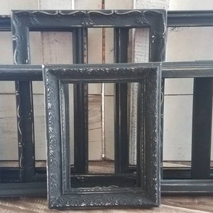 May include: A collection of black picture frames with ornate and simple designs. The frames are arranged in a group, showcasing various shapes and sizes. The frames have a distressed, vintage look.