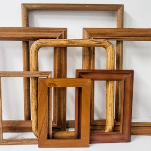 May include: A collection of wooden picture frames in various sizes and shades of brown. The frames are rectangular, with some featuring decorative edges. The arrangement includes both empty and curved frames, showcasing a range of styles.
