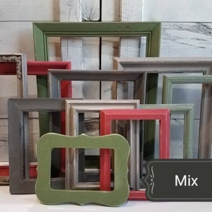 May include: A collection of various sized, colorful picture frames. The frames are painted in shades of red, green, gray, and white. A black sign with the word "Mix" is in the lower right corner. The frames are arranged in front of a white wooden background.