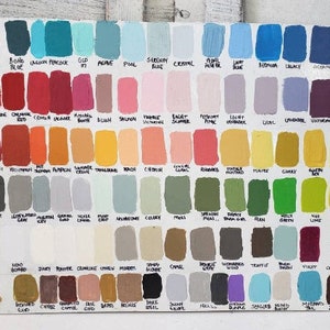 May include: A wooden board displays a wide array of paint color swatches. The samples are arranged in rows and columns, each labeled with a unique name. Colors range from blues and greens to reds, yellows, and purples, offering a comprehensive palette.