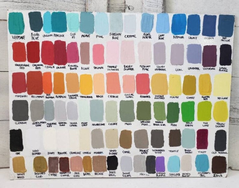 May include: A wooden board displays a wide array of paint color swatches. The samples are arranged in rows and columns, each labeled with a unique name. Colors range from blues and greens to reds, yellows, and purples, offering a comprehensive palette.