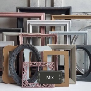 May include: A collection of various picture frames in different shapes, sizes, and colors. The frames include rectangular, oval, and circular designs, with colors like pink, gray, and brown. A small sign with the word "Mix" is visible.