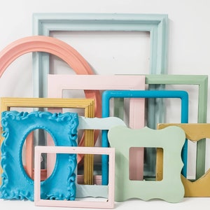 May include: A collection of colorful picture frames in various shapes and sizes. The frames are painted in pastel shades of pink, blue, green, and yellow. Some frames have ornate details, while others are simple and modern.