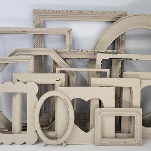 May include: A collection of various off-white picture frames in different shapes and sizes. The frames include rectangular, oval, and heart-shaped designs, with distressed edges. Some frames have decorative details.