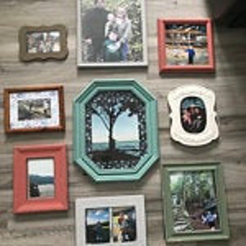 May include: A collection of framed photographs in various shapes and sizes. Frames include rectangular, octagonal, and ornate designs, with colors like brown, red, green, and white. The photos depict landscapes and people.