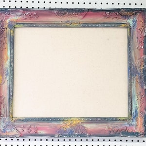 Peut inclure: Cadre photo rectangulaire orn&eacute; avec une finition vieillie. Le cadre pr&eacute;sente un m&eacute;lange de couleurs, dont le rose, le bleu, le jaune et le gris, avec des sculptures florales et des volutes d&eacute;taill&eacute;es. Le centre est de couleur beige clair.