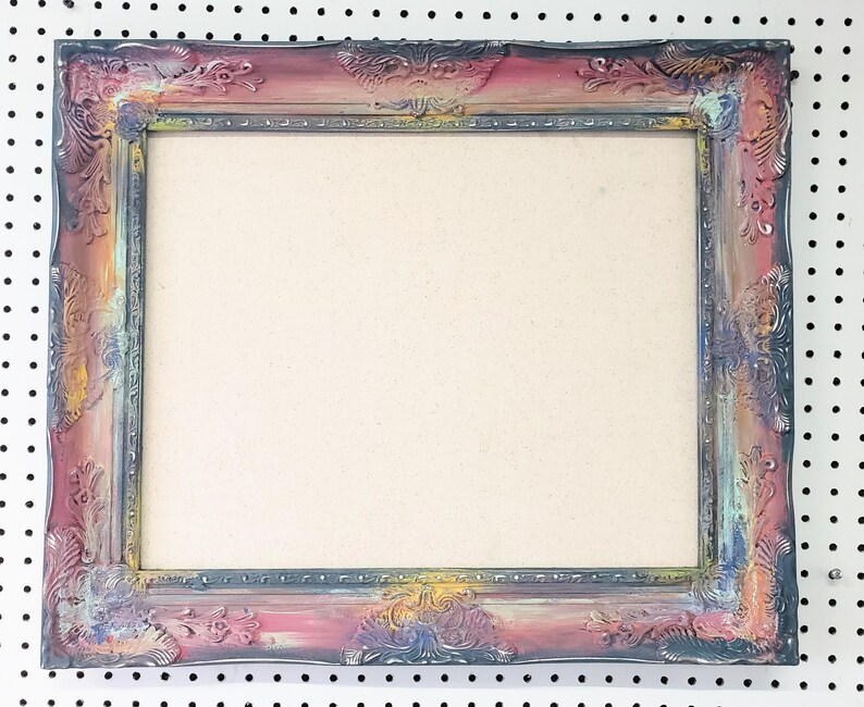 Peut inclure: Cadre photo rectangulaire orn&eacute; avec une finition vieillie. Le cadre pr&eacute;sente un m&eacute;lange de couleurs, dont le rose, le bleu, le jaune et le gris, avec des sculptures florales et des volutes d&eacute;taill&eacute;es. Le centre est de couleur beige clair.