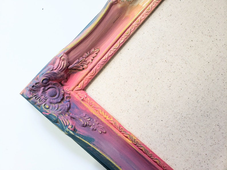 Peut inclure: Un coin d'un cadre photo d&eacute;coratif et orn&eacute;. Le cadre est peint avec un d&eacute;grad&eacute; de couleurs, notamment du rose, du violet, du bleu et de l'or. Le cadre pr&eacute;sente des motifs floraux et des volutes d&eacute;taill&eacute;s. Le fond est une toile.