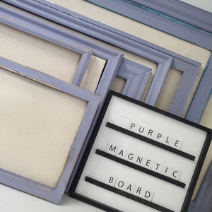 May include: A collection of various sized, light purple picture frames with a distressed finish. A black magnetic board displays the words "PURPLE MAGNETIC BOARD" in white letters. The frames are arranged on a neutral background.