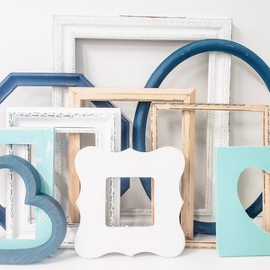 May include: A collection of various decorative picture frames in different shapes and colors. The frames include white, blue, and natural wood tones, with some featuring distressed finishes. There is a heart-shaped frame and a square frame with a heart cutout.