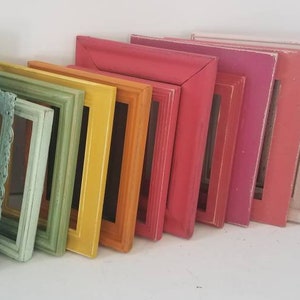 May include: A collection of colorful picture frames in various sizes and shades, including blue, green, yellow, orange, pink, and white. The frames are leaning against a white surface, showcasing a range of vibrant colors and styles.