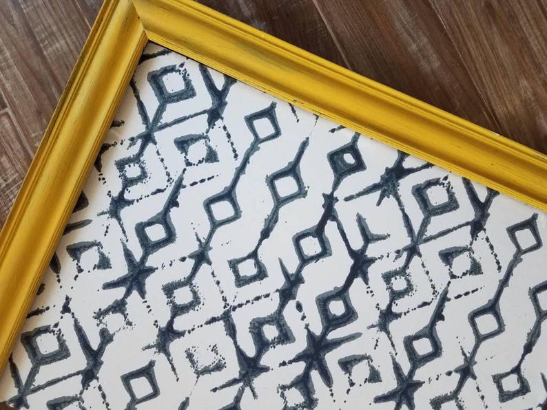 May include: A framed print with a yellow painted wooden frame. The print features a repeating pattern of dark blue diamond shapes on a white background. The frame has a distressed finish, adding a vintage feel to the artwork.