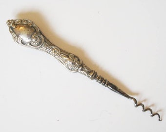 May include: Ornate silver corkscrew with a decorative handle featuring scrollwork and a heart-shaped design. The corkscrew has a long, slender body and a spiral worm for extracting corks from bottles. A vintage barware item.