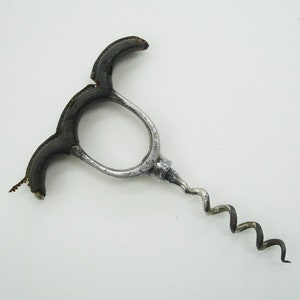 May include: A vintage corkscrew with a silver metal frame and a dark brown handle. The corkscrew has a spiral worm and a circular handle design. The handle is made of a dark brown material, and the metal frame has a worn appearance.