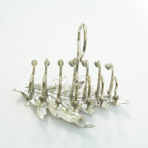 Könnte beinhalten: Silberfarbenes Metall-Servierstück in Blattform mit sechs gebogenen Haken und einem Griff. Das Blattdesign weist detaillierte Adern auf. Die Haken sind gleichmäßig am Blattrand angeordnet.