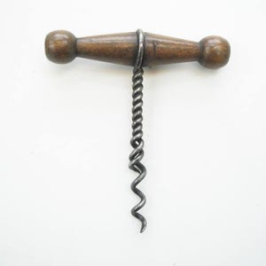 May include: A vintage corkscrew with a wooden handle and a twisted metal worm. The handle is a medium brown colour, and the metal is a dark grey. The corkscrew is designed for removing corks from wine bottles.