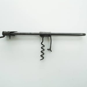 May include: A vintage, dark metal corkscrew with a long, cylindrical body. It features a worm, a lever, and a small blade. The corkscrew is designed for removing corks from bottles. The tool is set against a white background.