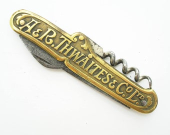 May include: Antique folding corkscrew with a brass handle and a steel blade. The handle is engraved with the text "A & R. THWAITES & CO. LTD." The corkscrew is open, revealing the blade and the corkscrew.