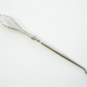 May include: A silver crochet hook with a textured handle and a small hole. The hook features a long, slender shaft and a curved end. The handle has a decorative pattern.