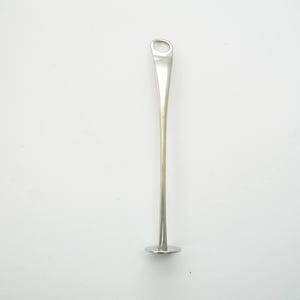 May include: A silver kitchen utensil with a long, thin handle and a small, circular base. The handle has a loop at the top. The tool is designed for stirring or mixing ingredients.