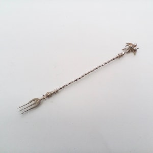Op de afbeelding: Een zilveren barlepel met een gedraaide steel, een drietandige vork aan één uiteinde en een decoratief engelenfiguur aan de andere kant. De lepel is ontworpen voor het mixen van cocktails en andere dranken.