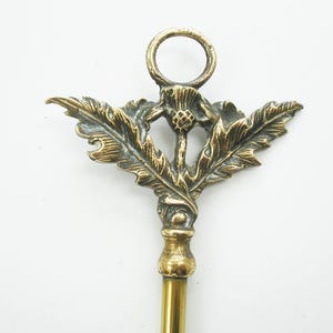 May include: A vintage brass letter opener with a thistle design. The opener features a detailed thistle emblem with leaves and a ring at the top. The handle is a simple, elongated shape.