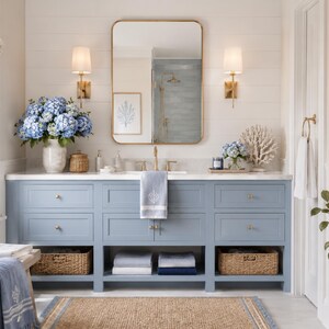 May include: A bathroom vanity in light blue with a white countertop, gold hardware, and a rectangular mirror. The vanity features drawers, open shelving with woven baskets, and folded towels. Blue hydrangeas and coral decor accent the space.