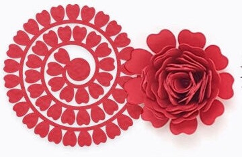 Op de afbeelding: Twee rode papieren bloemdecoraties. E&eacute;n is een gelaagde roos en de andere is een cirkelvormig ontwerp met hartvormige uitsparingen. Beide staan op een witte achtergrond. De roos heeft meerdere lagen bloemblaadjes.
