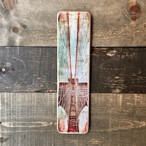 K&ouml;nnte beinhalten: Ein Vintage-Bild einer Br&uuml;cke in Rot-, Wei&szlig;- und Blaut&ouml;nen. Das Bild ist auf einer Holztafel mit einer abgenutzten Oberfl&auml;che gedruckt. Der Text "and I" ist auf der Tafel sichtbar.